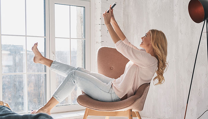 Young woman leaning back in chair playfully, smiling at cell phone camera.