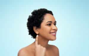 african american woman with bare shoulders showing her ear over blue background