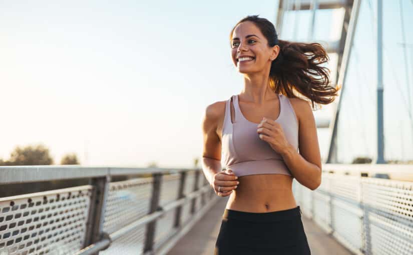 Smiling woman in athletic wear jogging outdoors, representing an active lifestyle and body-contouring goals.